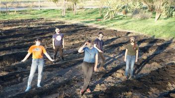 4 maske student interns stand in the empty soil of the food justice farm 